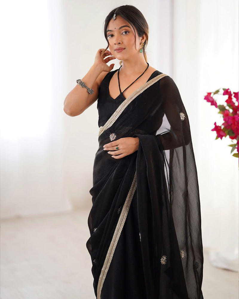Woman wearing a black saree with gold border against a white background